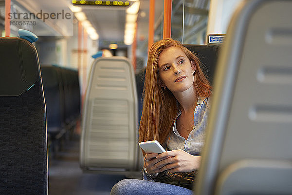 Nachdenkliche Frau mit Smartphone im Zug sitzend