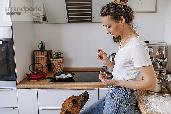 Schöne Frau mit unordentlichen Händen  die den Hund ansieht  während sie in der Küche steht