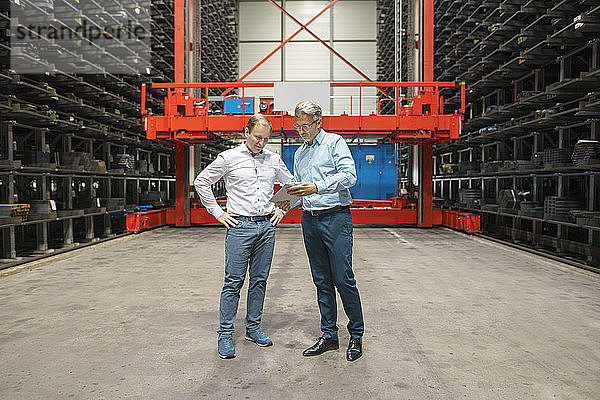 Zwei Geschäftsleute mit Tablet in einem Hochregallager einer Fabrik
