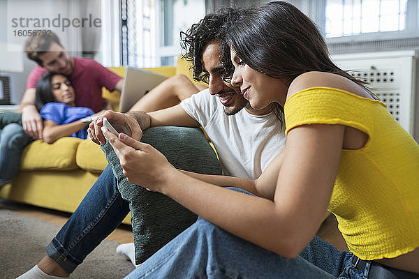 Junges Paar teilt sich einen digitalen Tisch  während sich Freunde im Wohnzimmer zu Hause entspannen