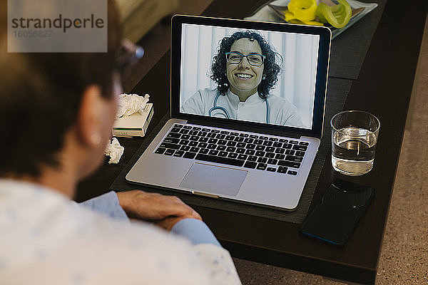 Lächelnder Arzt bei einem Videogespräch mit einer kranken älteren Frau über einen Laptop