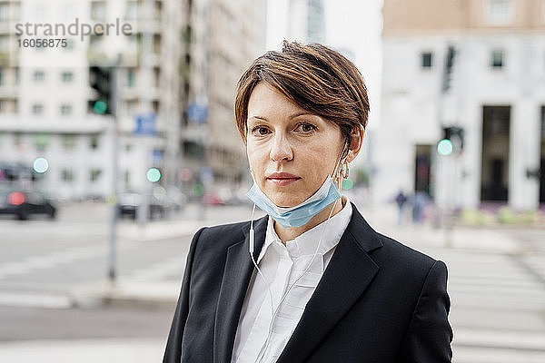 Nahaufnahme einer selbstbewussten Geschäftsfrau mit Maske vor einem Gebäude in der Stadt