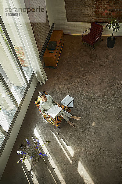 Älterer Mann sitzt auf einem Stuhl in einer Dachgeschosswohnung und liest Zeitung