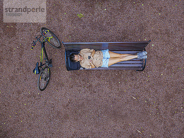 Luftaufnahme einer Frau  die ein Smartphone benutzt  während sie auf einer Parkbank liegt