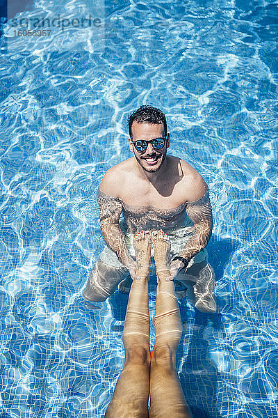 Mann mit Sonnenbrille hält Beine einer Frau im Schwimmbad