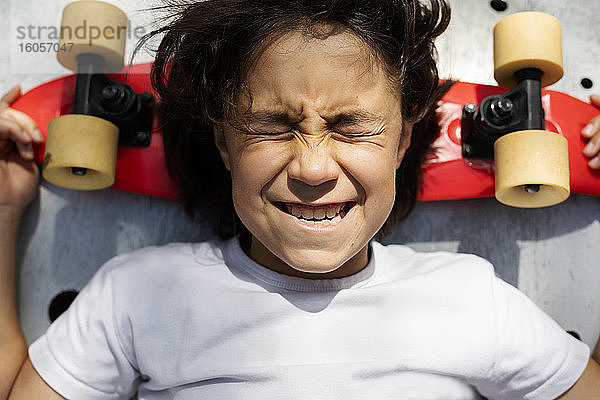 Nahaufnahme eines Jungen mit geschlossenen Augen  der ein Gesicht macht  während er auf einem Skateboard liegt