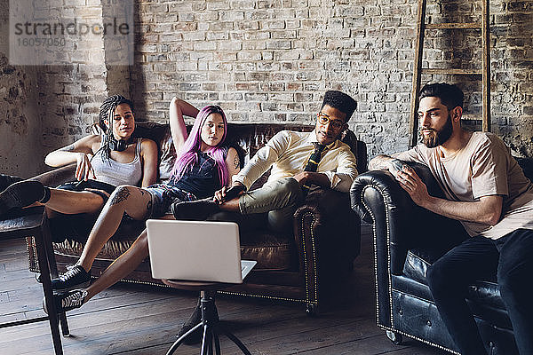 Eine Gruppe von Freunden sitzt auf einem Sofa in einem Loft und schaut auf einen Laptop