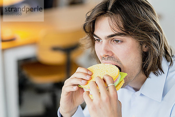 Nahaufnahme eines Geschäftsmannes  der einen Schwammtuch-Burger in einem Café isst