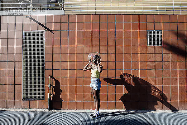 Junge Frau hält Glasbehälter über den Kopf  während sie auf dem Bürgersteig in der Stadt steht