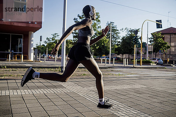 Weibliche Athletin hört Musik über Kopfhörer beim Laufen auf der Straße in der Stadt