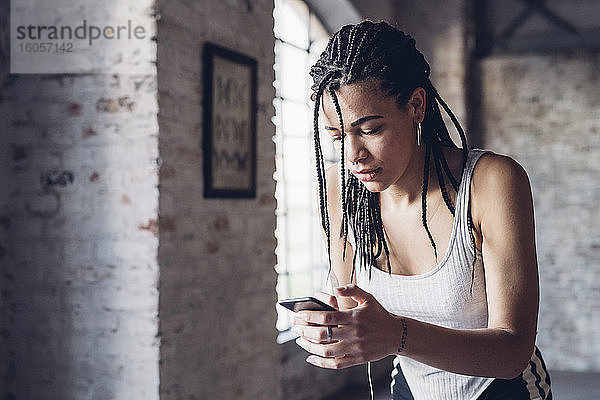 Stilvolle junge Frau benutzt Smartphone im Loft