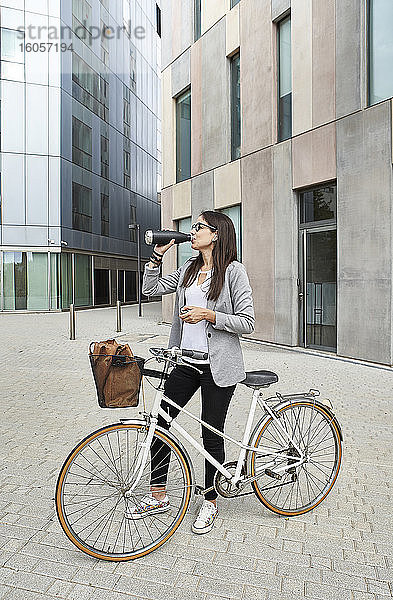 Geschäftsfrau trinkt Wasser  während sie mit dem Fahrrad auf der Straße steht