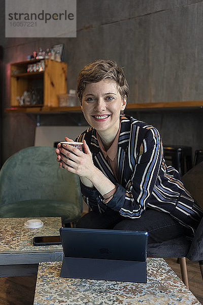 Porträt eines lächelnden Freiberuflers  der in einem Café mit digitalem Tablet und Smartphone sitzt