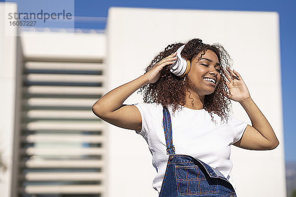 Glückliche Afro-Frau hört Musik über Kopfhörer beim Tanzen in der Stadt