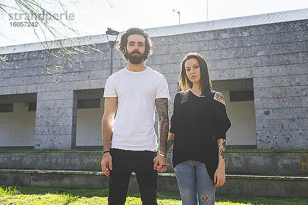 Paar hält sich an den Händen  während es an einem sonnigen Tag vor einem Gebäude steht