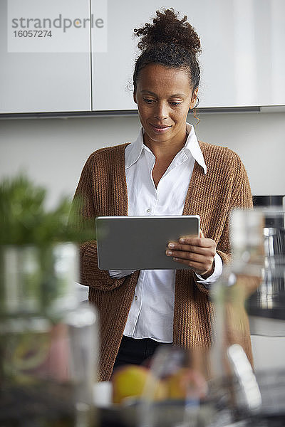 Porträt einer Geschäftsfrau  die in der Küche steht und ein digitales Tablet benutzt