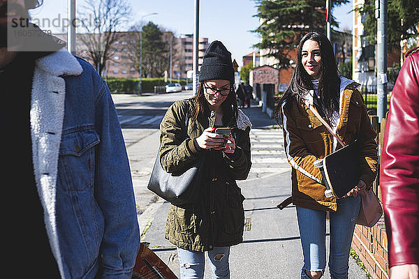 Frau benutzt Smartphone beim Spaziergang mit Freunden auf dem Bürgersteig in der Stadt