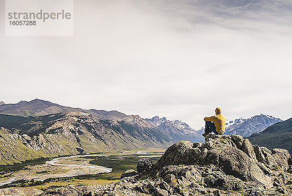 Männlicher Wanderer betrachtet die Aussicht  während er auf einem Felsen gegen den Himmel sitzt  Patagonien  Argentinien