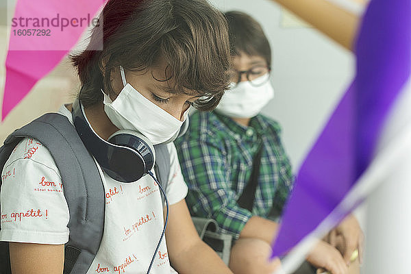 Nahaufnahme von Jungen mit Masken  die in der Schule sitzen und soziale Distanz wahren