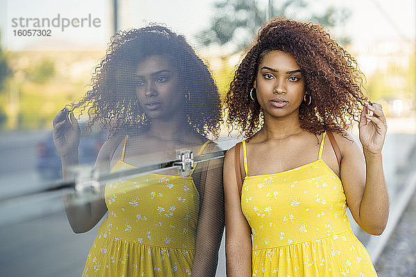 Ernste afroamerikanische Frau in gelbem Kleid steht vor einer Glaswand in der Stadt