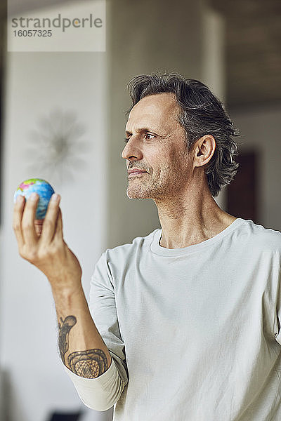 Älterer Mann hält Mini-Globus in einer Dachgeschosswohnung