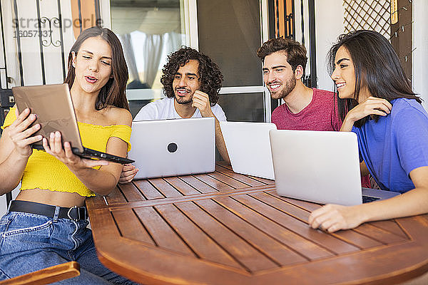 Junge Frau zeigt Laptop an lächelnde multiethnische Freunde  die am Tisch im Hinterhof sitzen