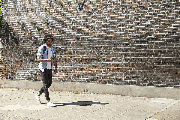 Junger Mann geht auf dem Bürgersteig und schaut auf sein Mobiltelefon  London  UK