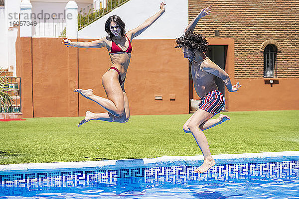 Glückliches junges Paar  das an einem sonnigen Tag in den Swimmingpool im Hinterhof springt