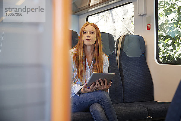 Nachdenkliche junge Frau  die ein digitales Tablet hält  während sie im Zug sitzt