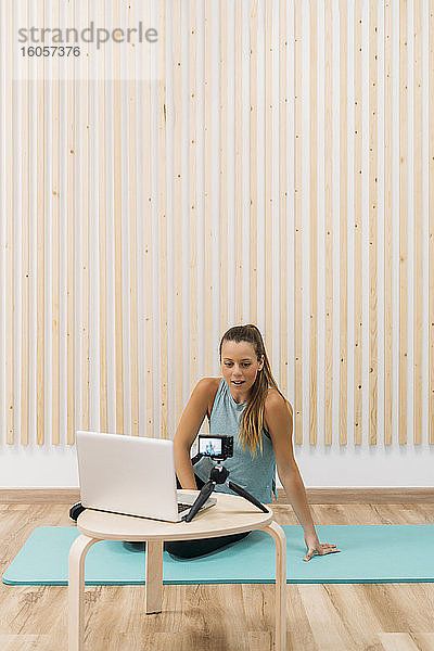 Sportliche Frau filmt sich selbst mit Kamera und Laptop