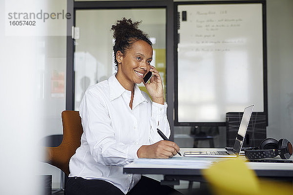 Porträt einer lächelnden Geschäftsfrau am Telefon  die am Schreibtisch im Büro sitzt