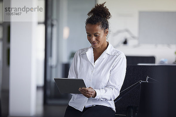 Porträt einer lächelnden Geschäftsfrau  die in einem modernen Büro ein digitales Tablet benutzt