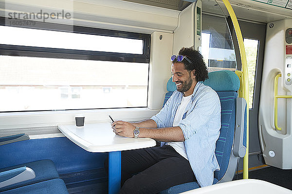 Glücklicher junger trendiger Mann  der sein Smartphone im Zug benutzt