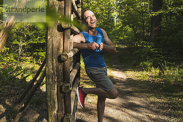 Glücklicher Mann  der wegschaut  während er mit einer Wasserflasche gegen ein Holz im Park steht