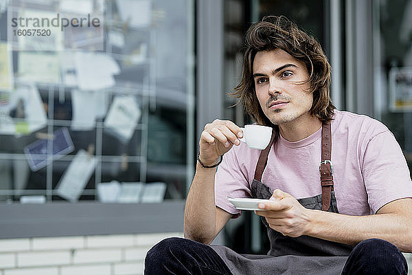 Nachdenklicher männlicher Barista mit Kaffee in der Hand vor einem Café