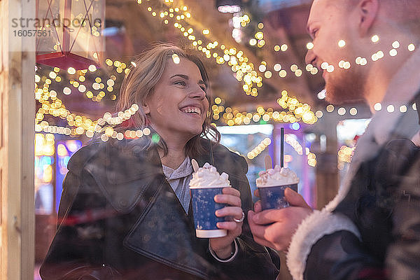 Nahaufnahme eines glücklichen Paares mit heißer Schokolade im Gespräch in einem Geschäft  gesehen durch ein Fenster