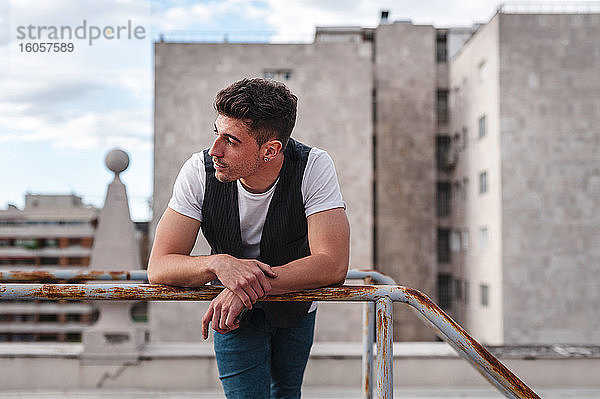 Nachdenklicher junger Mann steht am Geländer einer verlassenen Terrasse in der Stadt