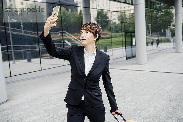 Geschäftsfrau  die ein Selfie mit ihrem Mobiltelefon macht  während sie auf einem Fußweg in der Stadt steht