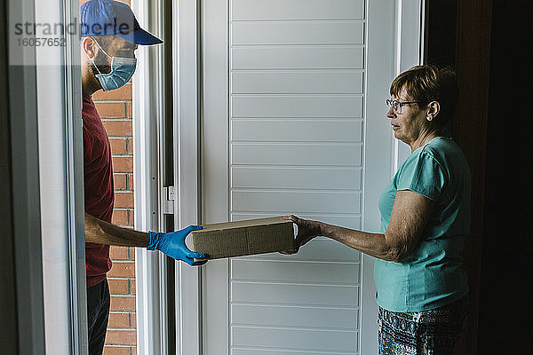 Postangestellte  die einer älteren Frau an der Haustür ein Paket übergibt  wird vom Coronavirus infiziert