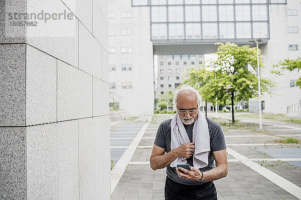 Älterer Mann mit Brille benutzt sein Smartphone  während er auf einem Fußweg in der Stadt steht