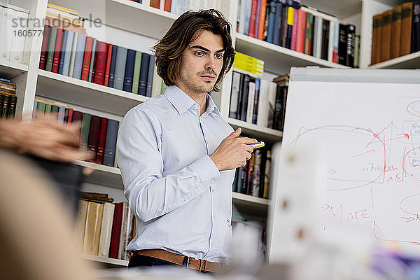 Selbstbewusster männlicher Fachmann  der in einer Besprechung im Büro Daten über ein Whiteboard erklärt