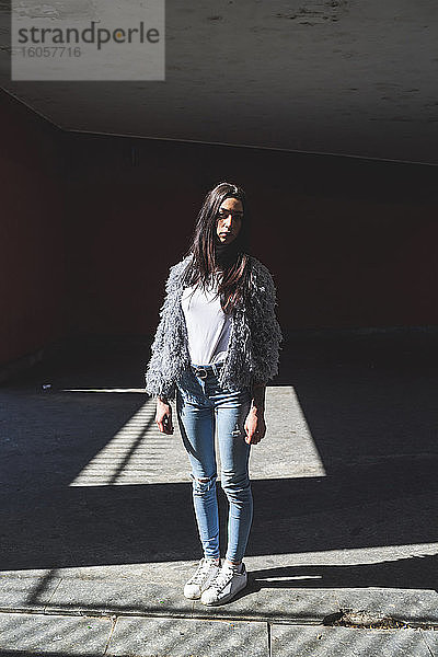 Junge Frau mit Jacke  die an einem sonnigen Tag vor einem Gebäude steht