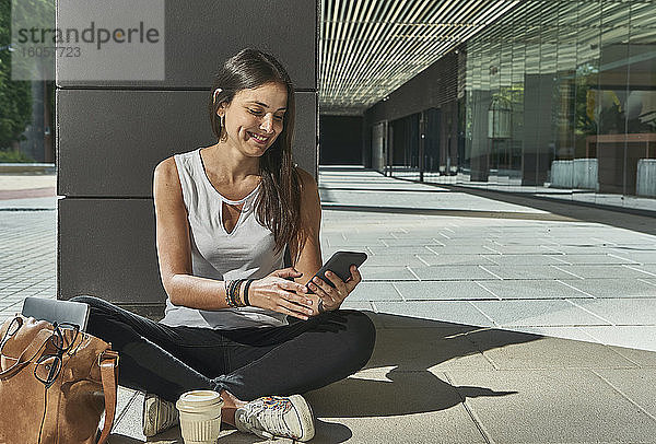 Geschäftsfrau  die ein Smartphone benutzt  während sie an einem sonnigen Tag auf der Kolonnade sitzt