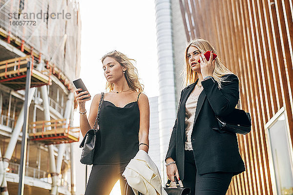 Weibliche Kollegen benutzen Smartphones  während sie an Gebäuden in der Stadt stehen