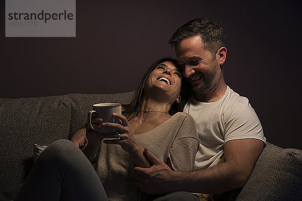 Verliebtes Paar lacht beim Entspannen auf dem Sofa an der Wand zu Hause