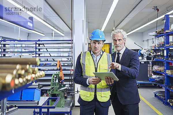 Vorgesetzter und männlicher Manager diskutieren über ein digitales Tablet in einer Fabrik