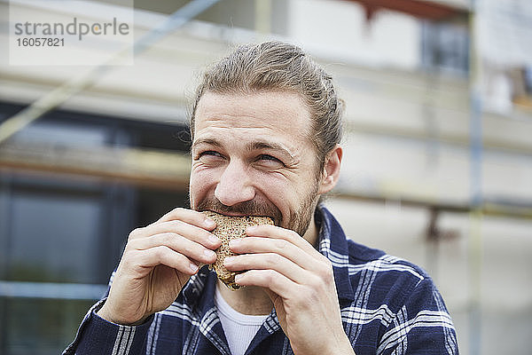 Porträt eines Arbeiters in der Mittagspause auf einer Baustelle  der ein Brot isst