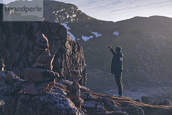 Junger Mann  der ein Selfie macht  während er auf einem felsigen Berg in Teriberka  Gebiet Murmansk  Russland  steht