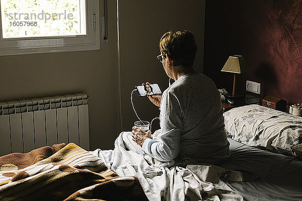 Frau im Ruhestand führt ein Videogespräch mit einem Arzt  während sie zu Hause im Schlafzimmer sitzt
