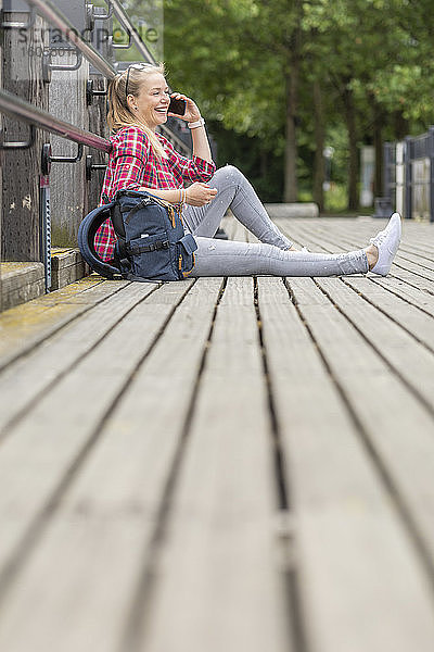 Mittlere erwachsene Frau  die über ein Smartphone spricht  während sie auf einer Brücke in der Stadt sitzt